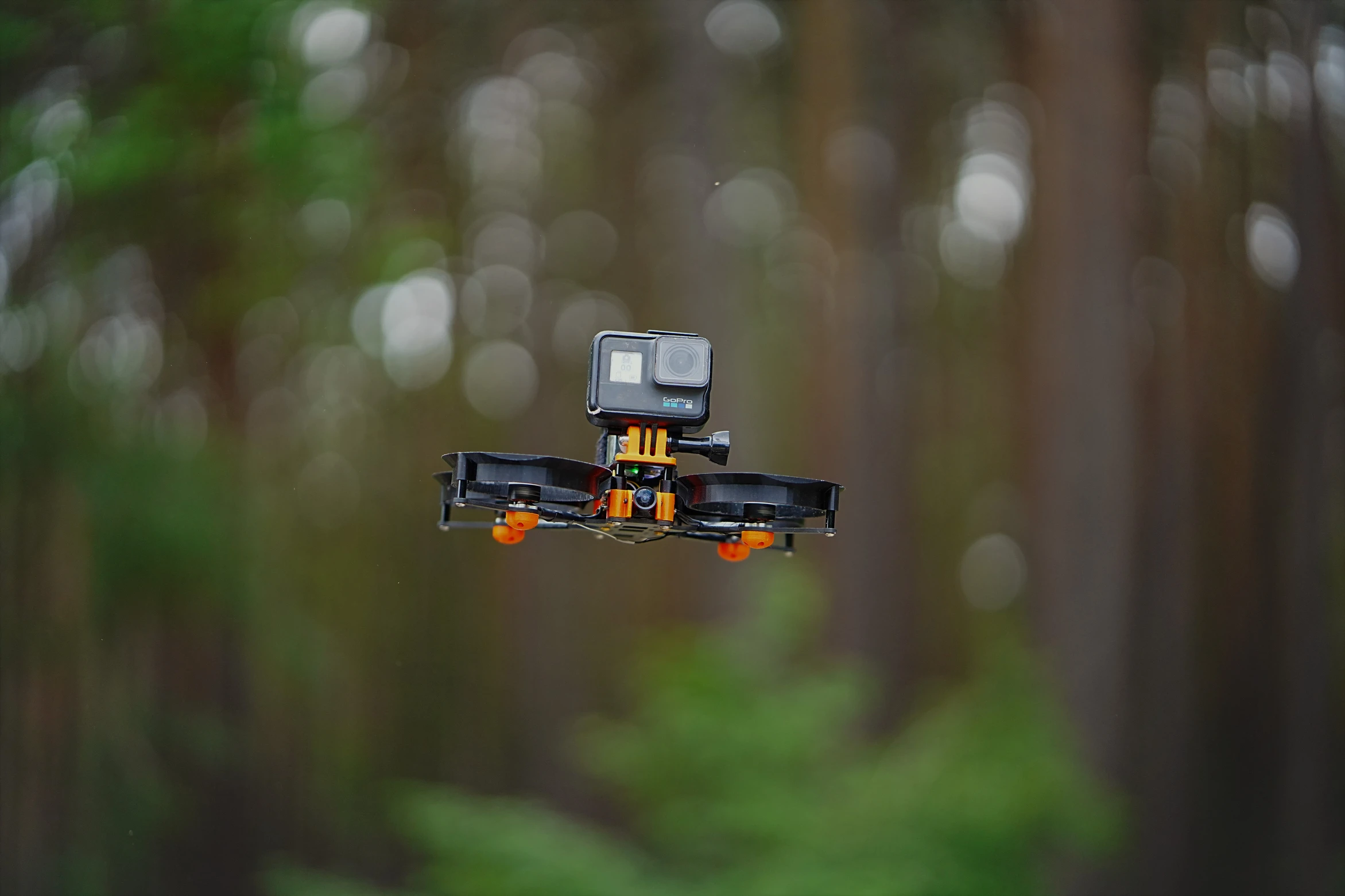 Cinewhoop with orange ducts and a mounted GoPro flying in the air